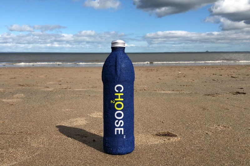 Uma garrafa azul com o logo da Ch2oose na praia